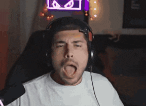 a man wearing headphones is covering his eyes with his hands while sitting in front of a neon sign with eyes .