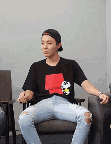 a young man is sitting in a chair wearing a snoopy t-shirt .