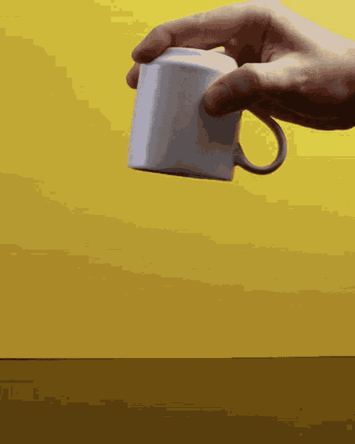 a person is holding a white coffee cup with a yellow background