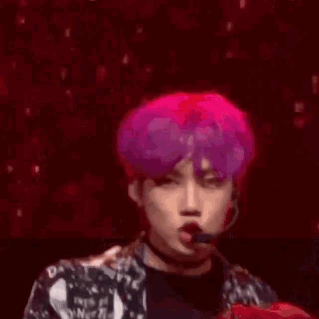 a man with purple hair is wearing a choker and a microphone while standing on a stage .