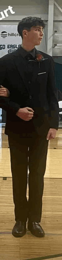 a young man in a black suit is standing on a basketball court