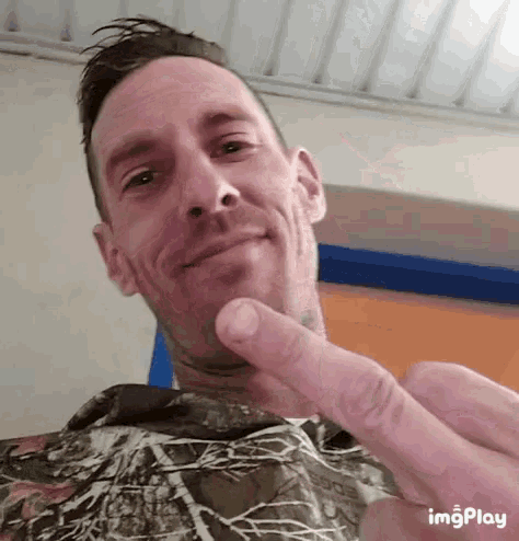 a man in a camo shirt is giving a peace sign with his finger
