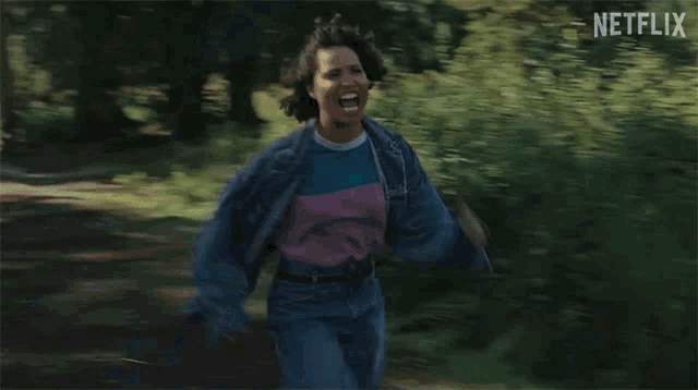 a woman in a denim jacket is running through a field .