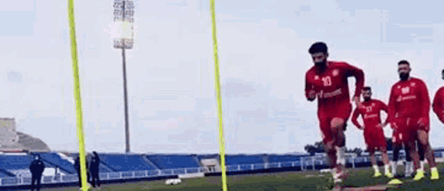 a soccer player in a red shirt is jumping over a yellow pole on a field .