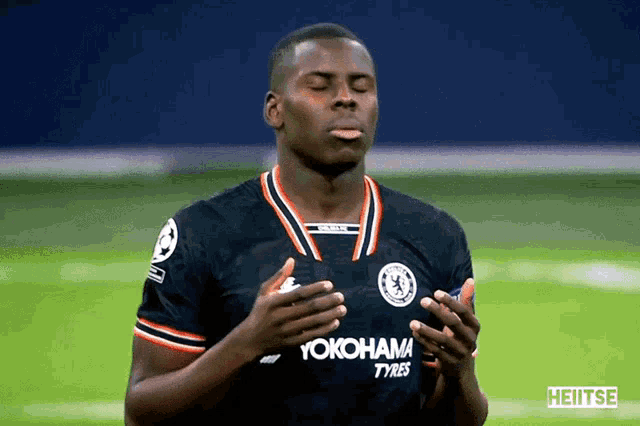 a soccer player wearing a yokohama tyres jersey prays with his eyes closed