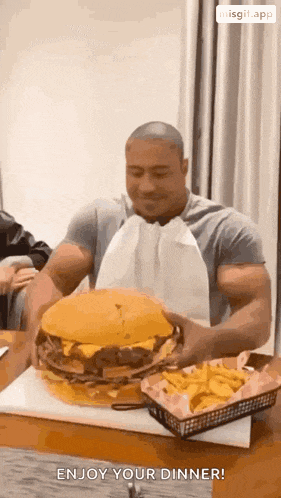 a muscular man is eating a very large hamburger and french fries .