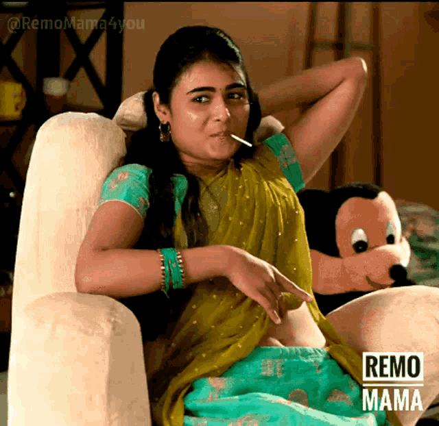 a woman in a sari is sitting in a chair with a stuffed mickey mouse in the background