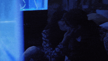 two women are sitting in a dark room looking at a blue screen