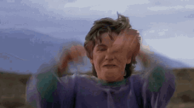 a man in a purple sweater is covering his face with his hands .