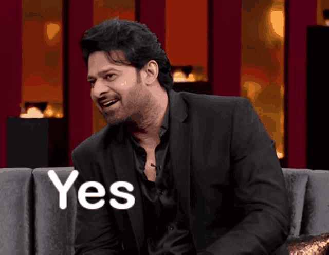 a man in a suit is sitting on a couch with the word yes behind him