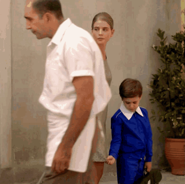 a man in a white shirt walks with a woman and a boy in blue