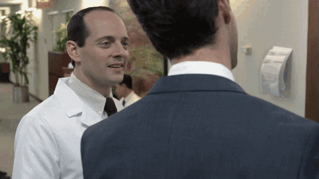 a man in a suit is talking to a doctor in a lab coat