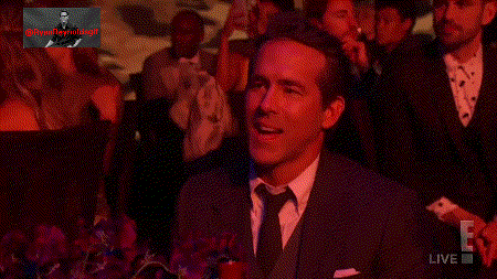 a man in a suit and tie smiles in front of a screen that says live