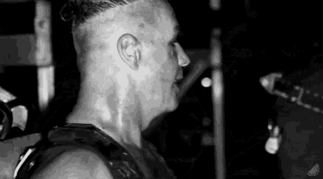a black and white photo of a man with a shaved head standing in a dark room .