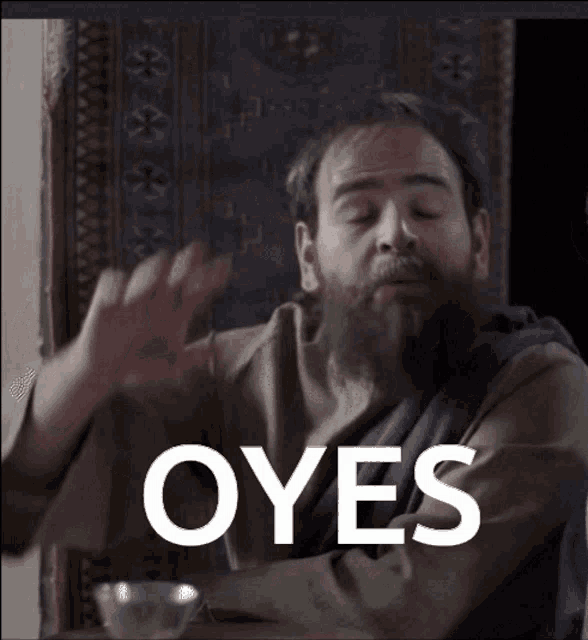 a man with a beard is sitting at a table with the word oyes written in white letters