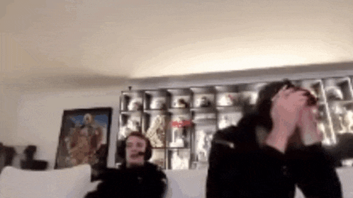 two people are sitting on a couch in a living room . one of the people is wearing headphones .