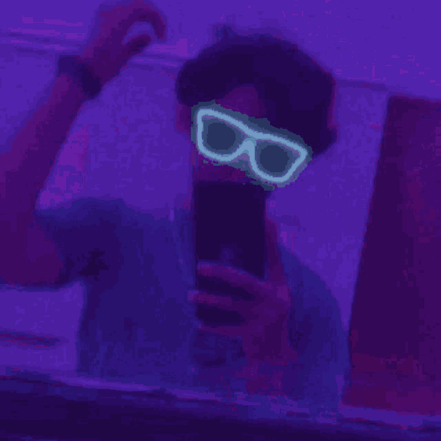 a man wearing glow in the dark sunglasses is taking a selfie with his phone .