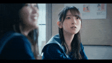 two girls are sitting in front of a wall with a picture of a man on it