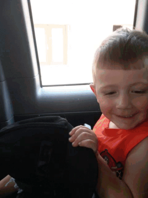 a young boy wearing an orange angry bird shirt is sitting in a car seat