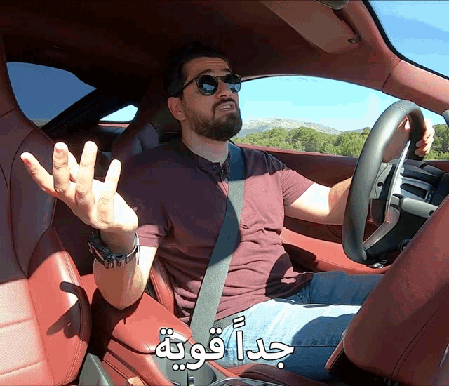 a man wearing sunglasses is sitting in a car with arabic writing behind him