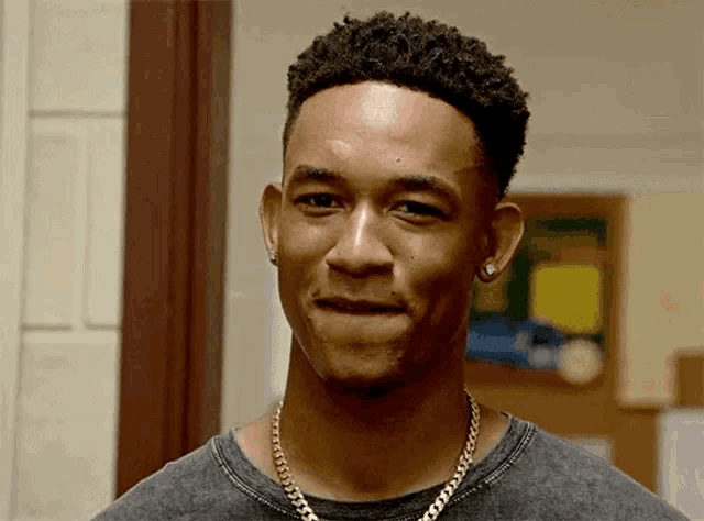 a young man wearing a necklace and earrings is smiling .