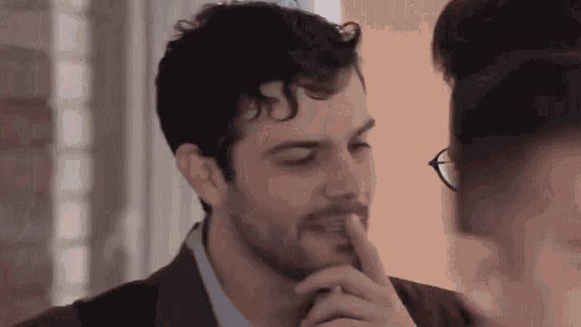 a man with a beard and glasses is holding his finger to his mouth