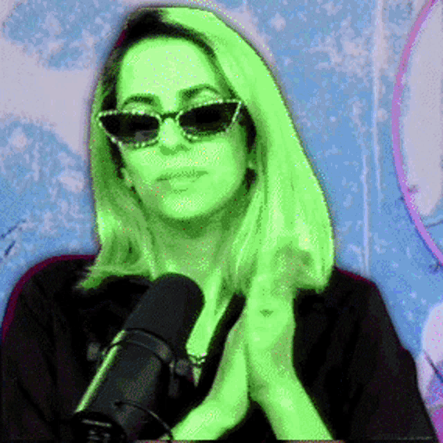 a woman wearing sunglasses and a black shirt is talking into a microphone