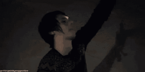 a woman in a black dress is standing in a dark room with her head down .
