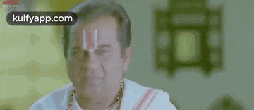 a man with a necklace on his neck is wearing a white shirt and a necklace on his forehead .