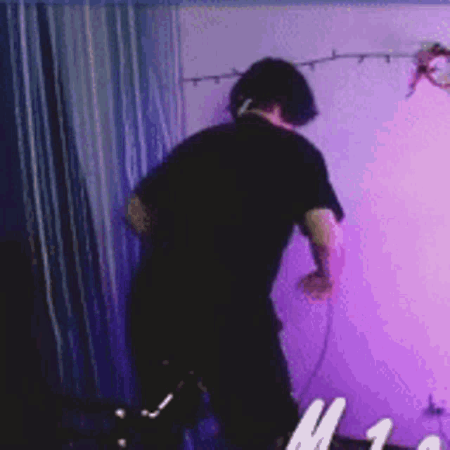 a man in a black shirt is standing in a room with purple lights on the wall .