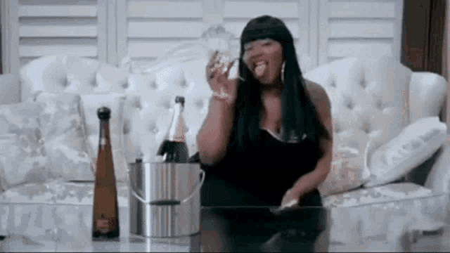 a woman is sitting on a couch with a bucket of champagne and a glass of wine .