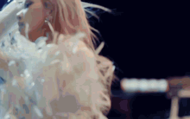 a woman in a white feathered dress is dancing on a stage in a dark room .