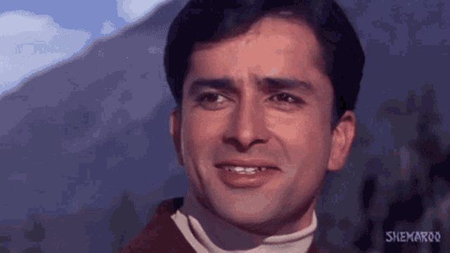 a man in a brown jacket and white turtleneck is smiling .