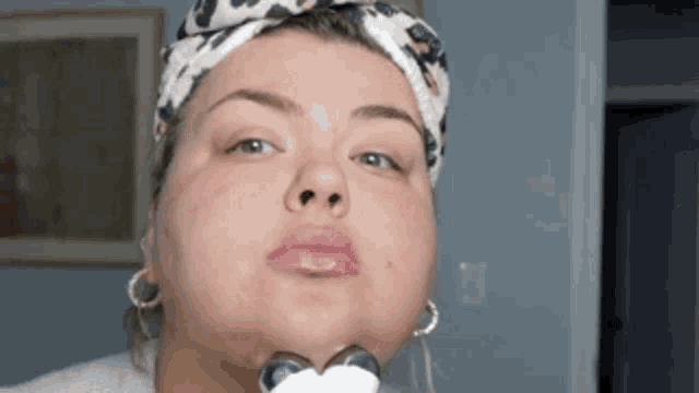 a woman wearing a headband and earrings is looking at her face in the mirror .