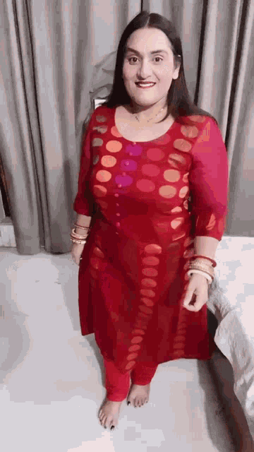 a woman in a red dress is standing in front of a curtain .