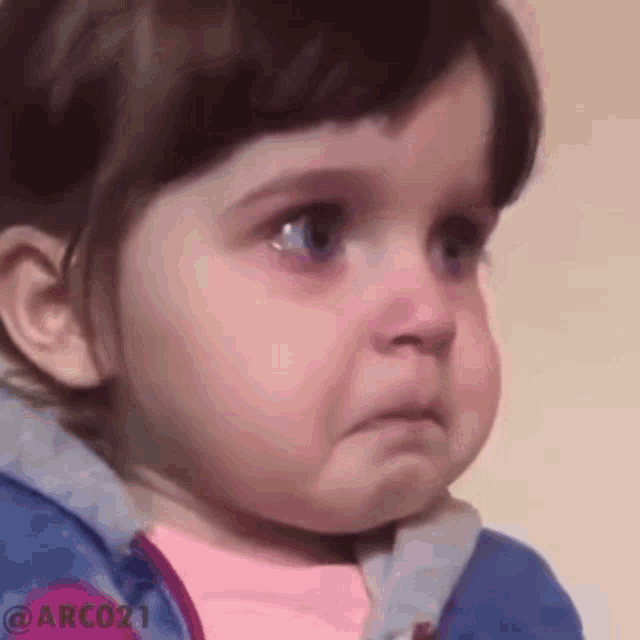 a baby girl is crying and making a funny face while wearing a blue jacket .