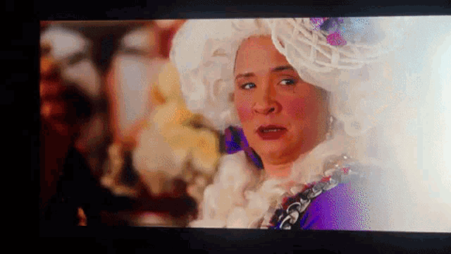 a woman in a white wig and purple dress on a screen