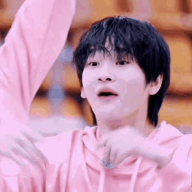 a young man wearing a pink hoodie is making a surprised face