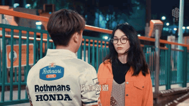 a man wearing a white rothmans honda shirt talks to a woman