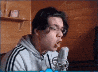 a young man is singing into a microphone while wearing glasses .