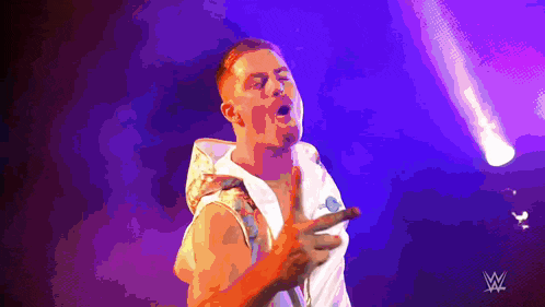 a man is standing in front of a purple background with a w logo on the bottom