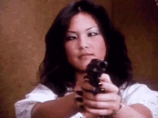 a woman is pointing a gun at the camera in a close up .
