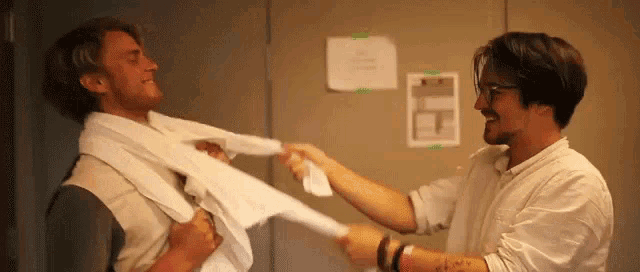 two men are holding towels around each other 's necks in a room .