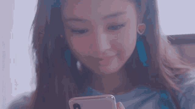 a woman is looking at her phone and smiling while wearing earrings .
