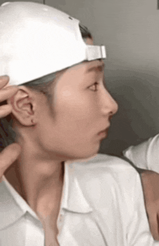 a woman wearing a white hat and a white shirt is being touched by another person .