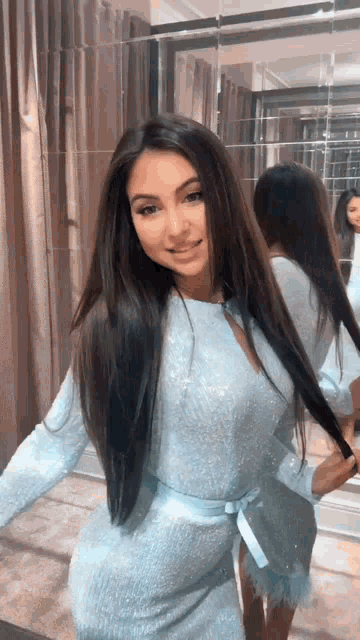 a woman in a light blue dress is standing in front of a mirror holding her hair