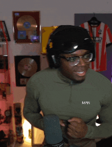 a man wearing headphones and glasses is standing in front of a microphone with a shirt hanging on the wall behind him