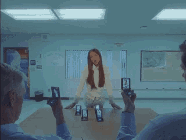 a woman in a white shirt is standing in front of a group of people holding flip phones