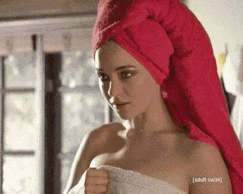 a woman with a red towel wrapped around her head is standing in front of a window .