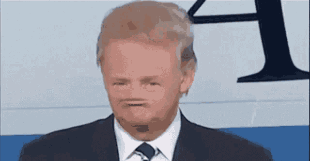 a man in a suit and tie is making a funny face in front of a sign .